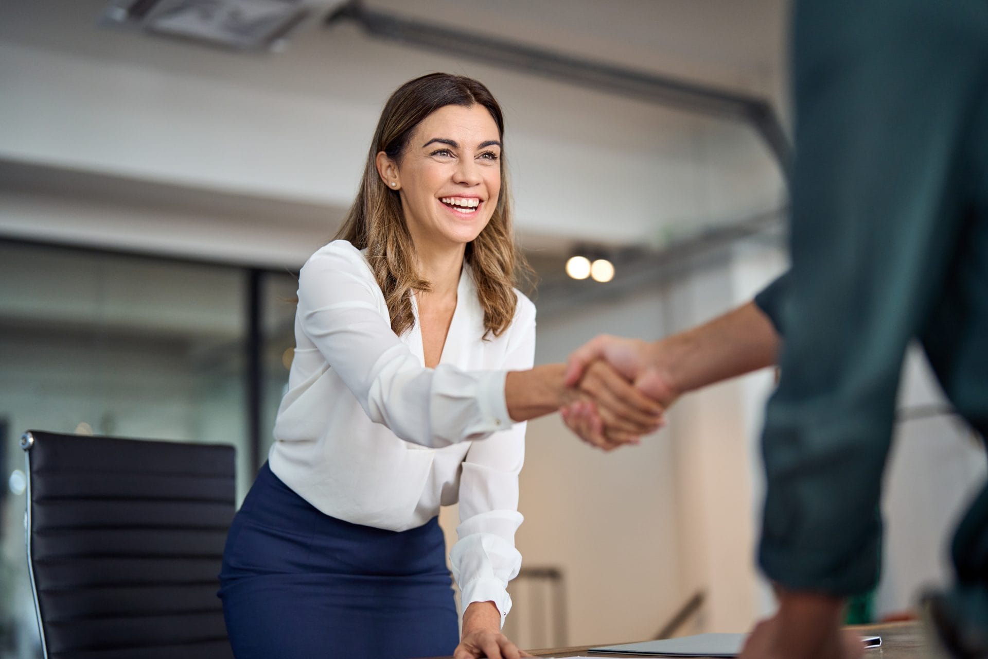 Smiling businesswoman in a white blouse shaking hands with a colleague at a desk