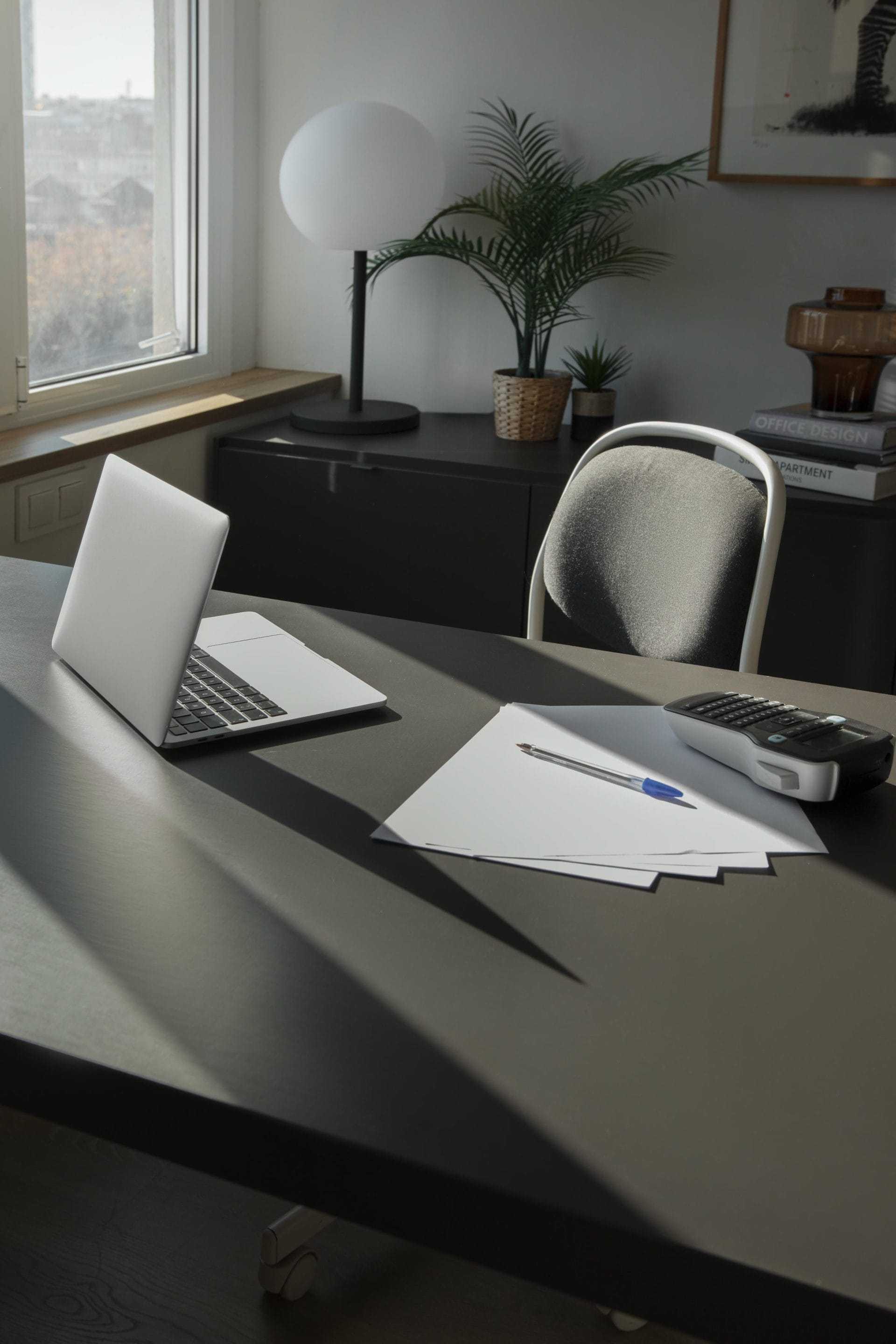 Modern office desk with an open laptop, calculator, and notepad lit by natural window light
