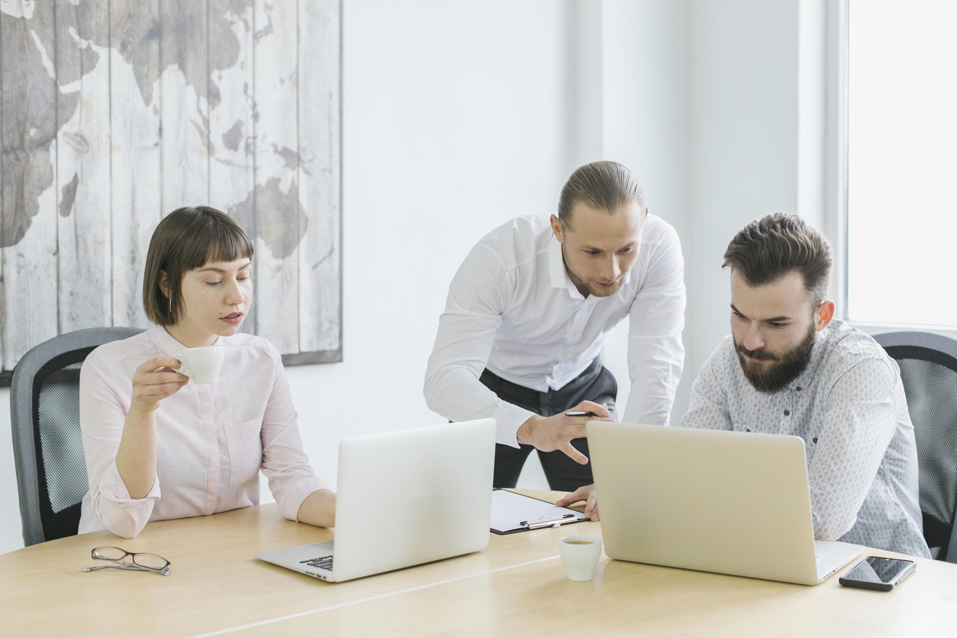 Three colleagues reviewing work on laptops together at a conference table in a bright office